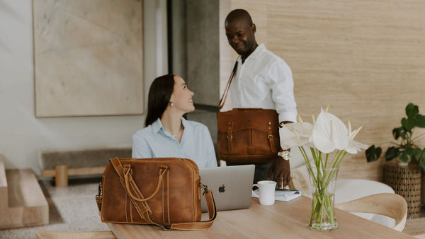 Two people in a modern office setting with a table, balvaro laptop bag, and flowers.