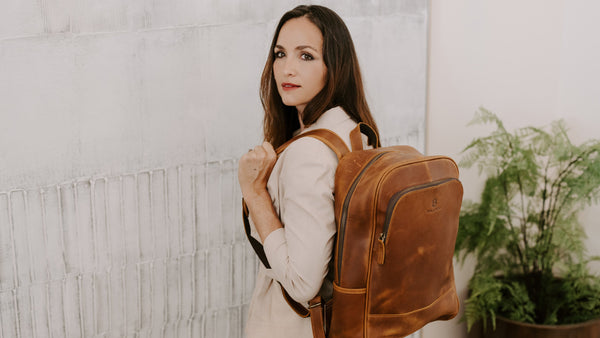Woman wearing a balvaro leather backpack against a light gray wall with a plant in the background.